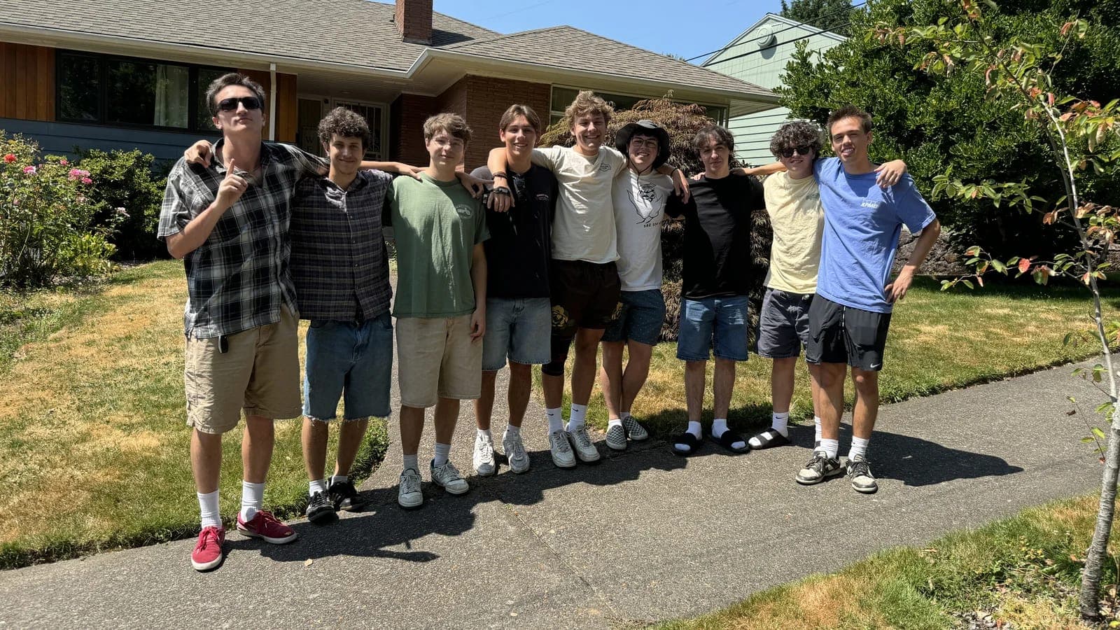 The friend group Declaration was built for, standing arm in arm on a driveway on a summer afternoon.