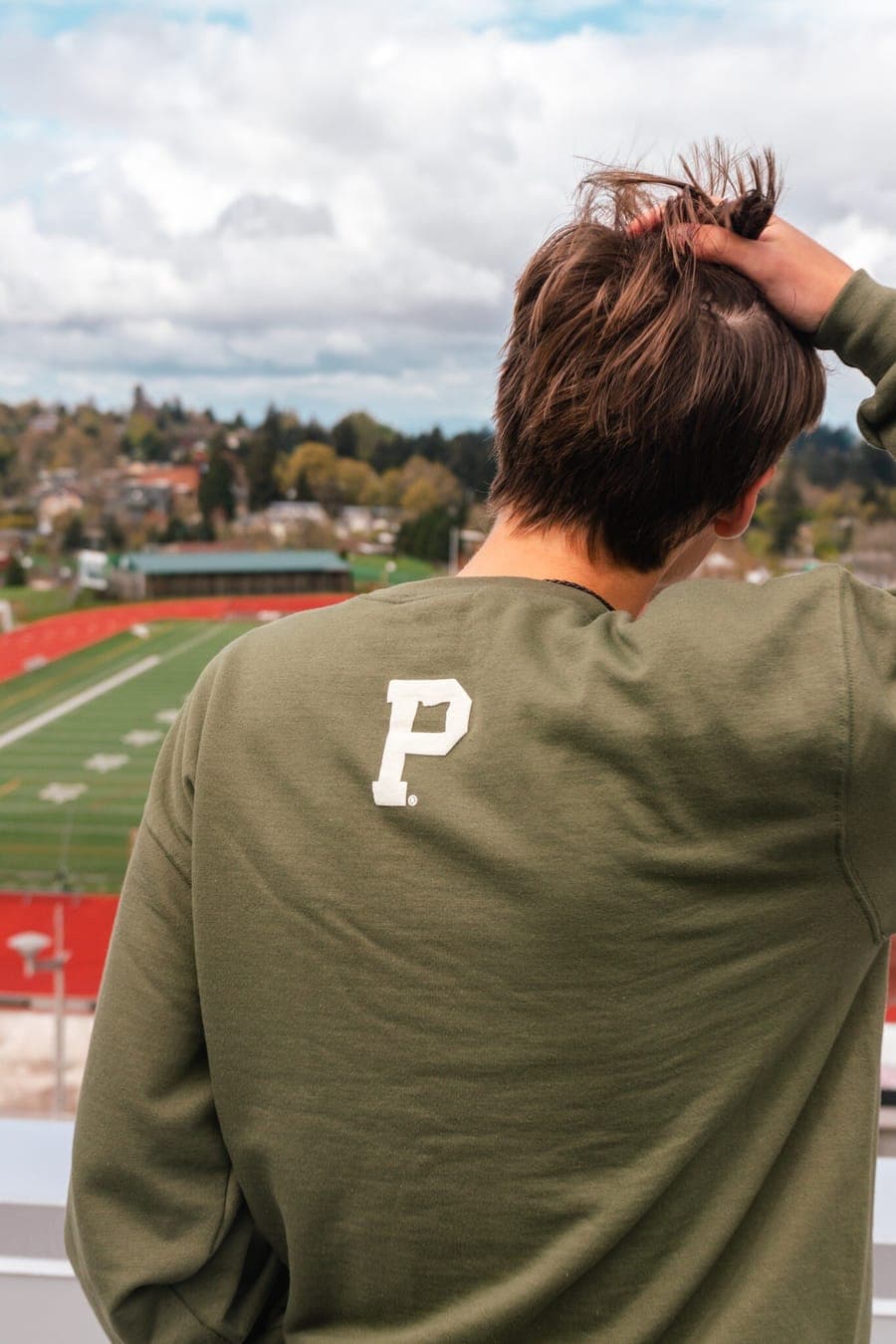 Back of the olive crewneck with the white Portland Gear P logo, overlooking the field